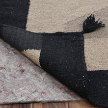 Load image into Gallery viewer, Close-up of a black and beige checkered rug with tassels on a wooden floor.
