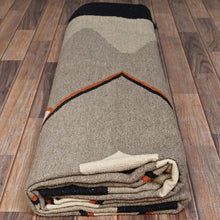 Load image into Gallery viewer, Folded blanket with geometric pattern on a wooden floor